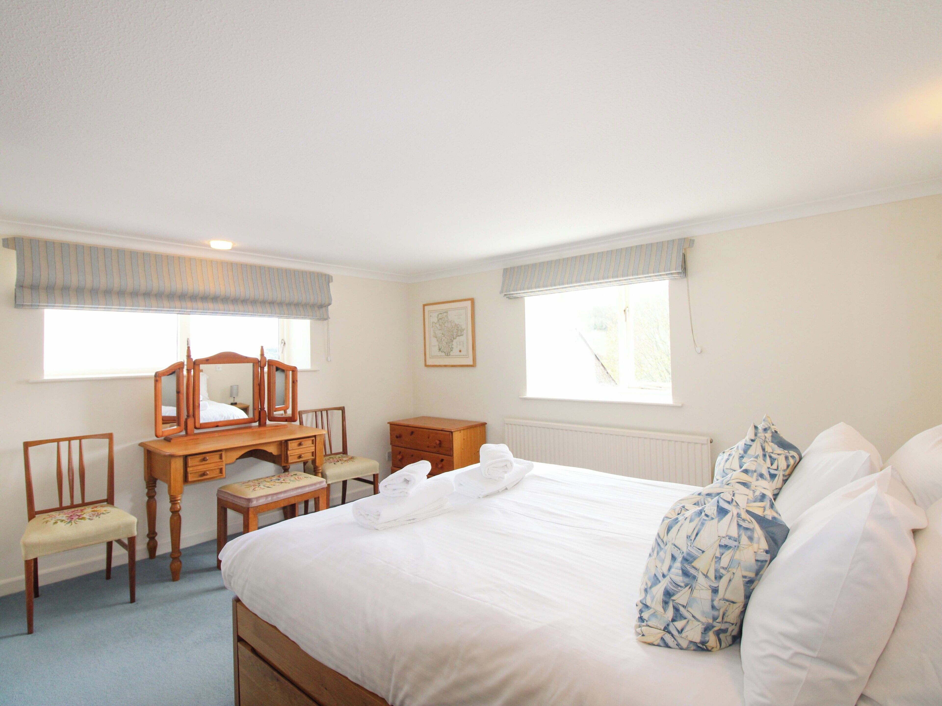 A bedroom with a bed, a wooden dresser, a chair, a desk, and a window with blinds.