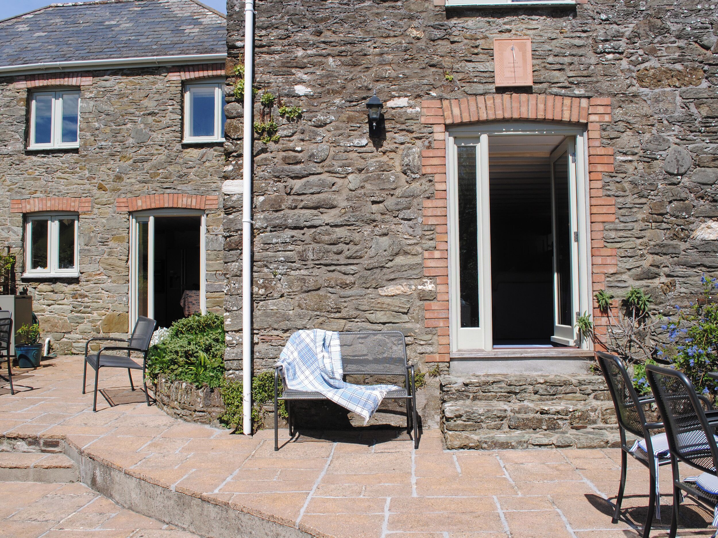A stone building with a patio area featuring a bench and chairs.