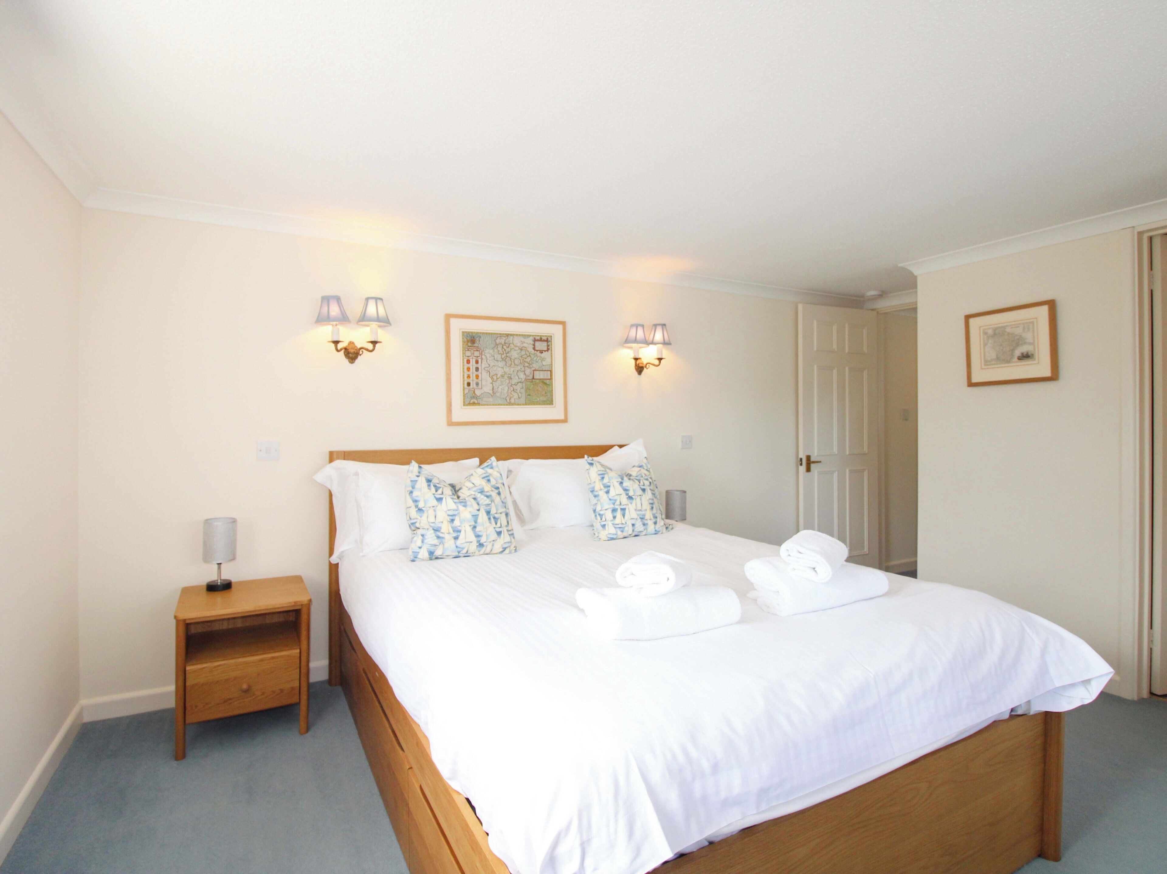 A neatly made bed with white linens and decorative pillows, a bedside table with a lamp, and wall-mounted light fixtures.