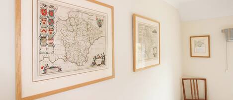 A room with two framed maps on the wall, a wooden chair, and a bed.