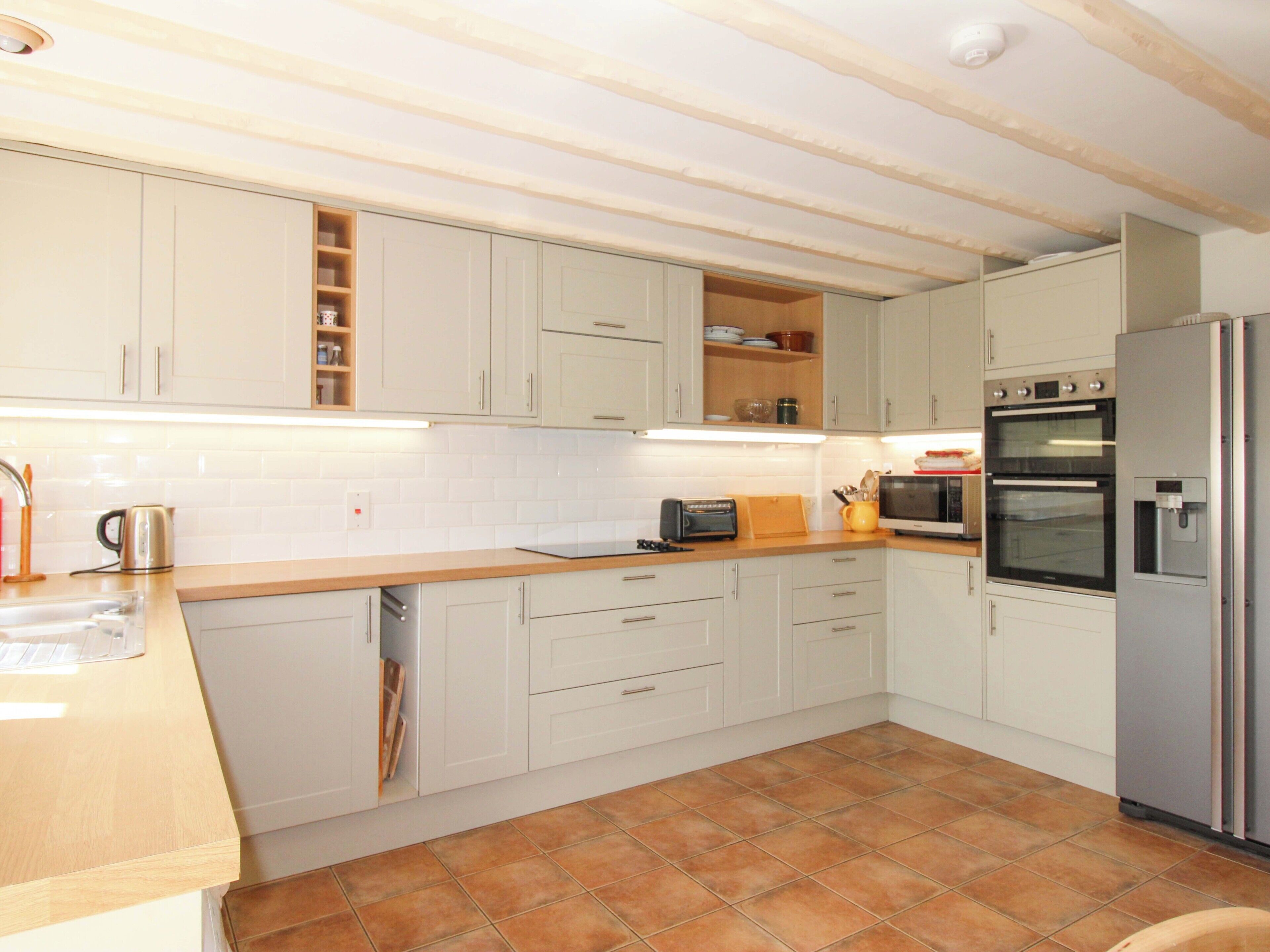A kitchen with white cabinets, a wooden countertop, a dishwasher, an oven, and a refrigerator.