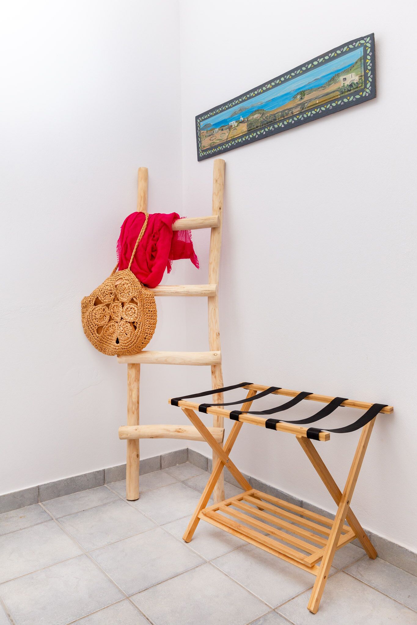 Un tendedero de madera con un paño negro, una cesta tejida y un paño rojo colgado en una escalera de madera contra una pared blanca.