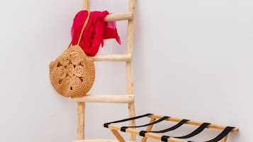 Un tendedero de madera con un paño negro, una cesta tejida y un paño rojo colgado en una escalera de madera contra una pared blanca.