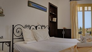 A bedroom with a bed, a bedside table, a wardrobe, a window with curtains, and a view of the outdoors. - Ailouros summer hotel (Naxos)
