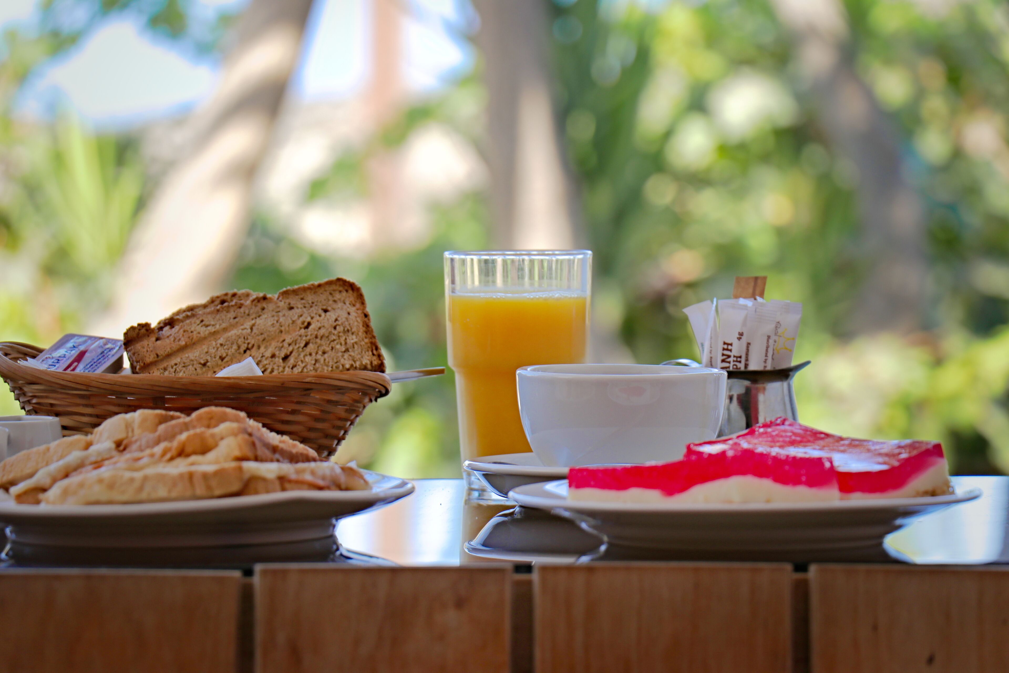 Une table de petit-déjeuner avec du pain, un verre de jus d’orange, une tasse et une assiette contenant une part de gâteau.