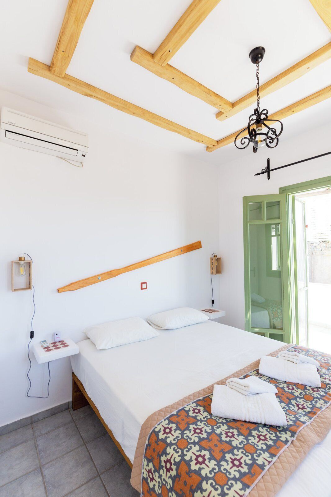 Un dormitorio con cama, mesita de noche, lámpara colgante, ventana y puerta verde.