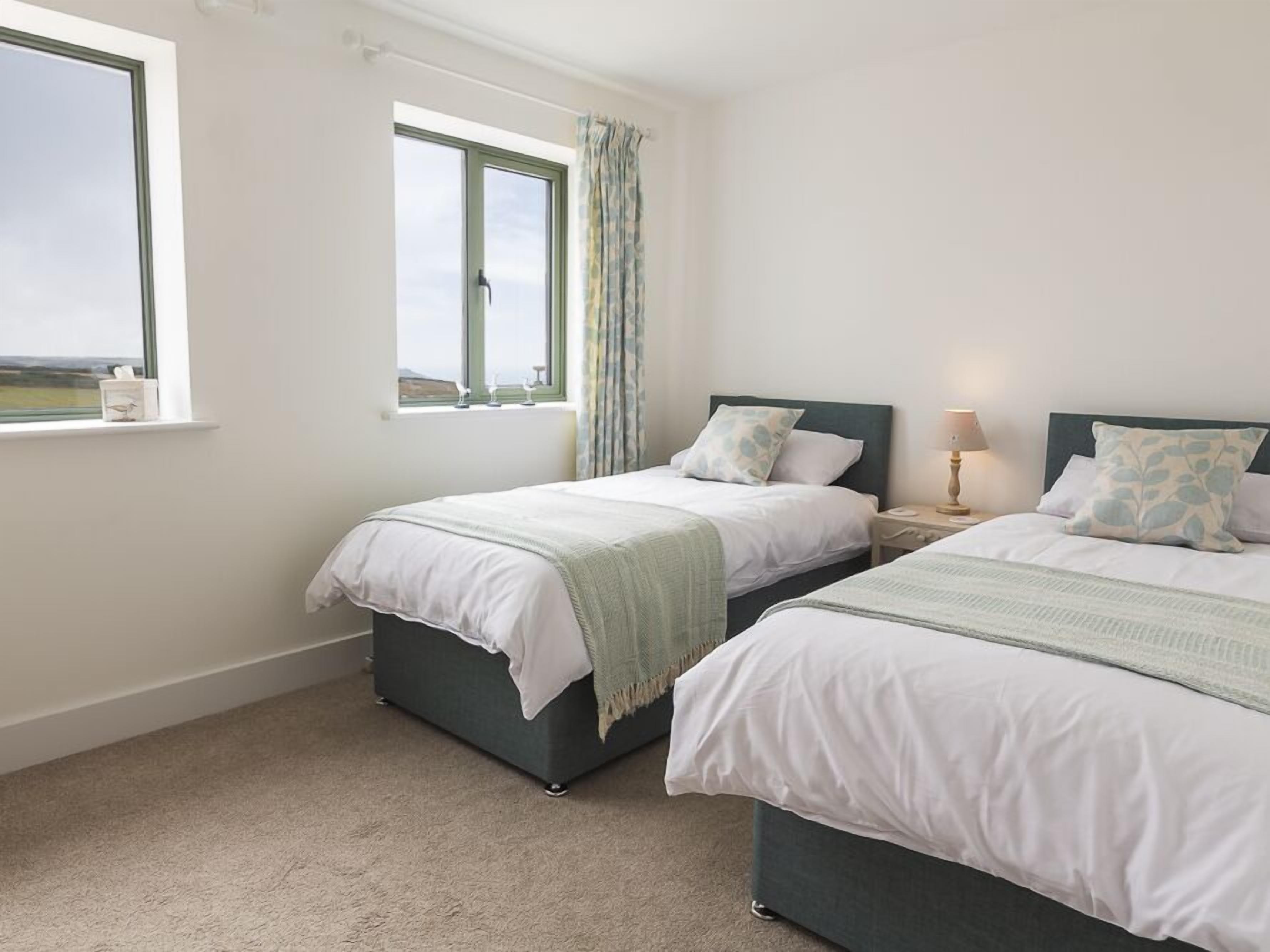 A bedroom with two beds, a window with a view, and a bedside table with a lamp.