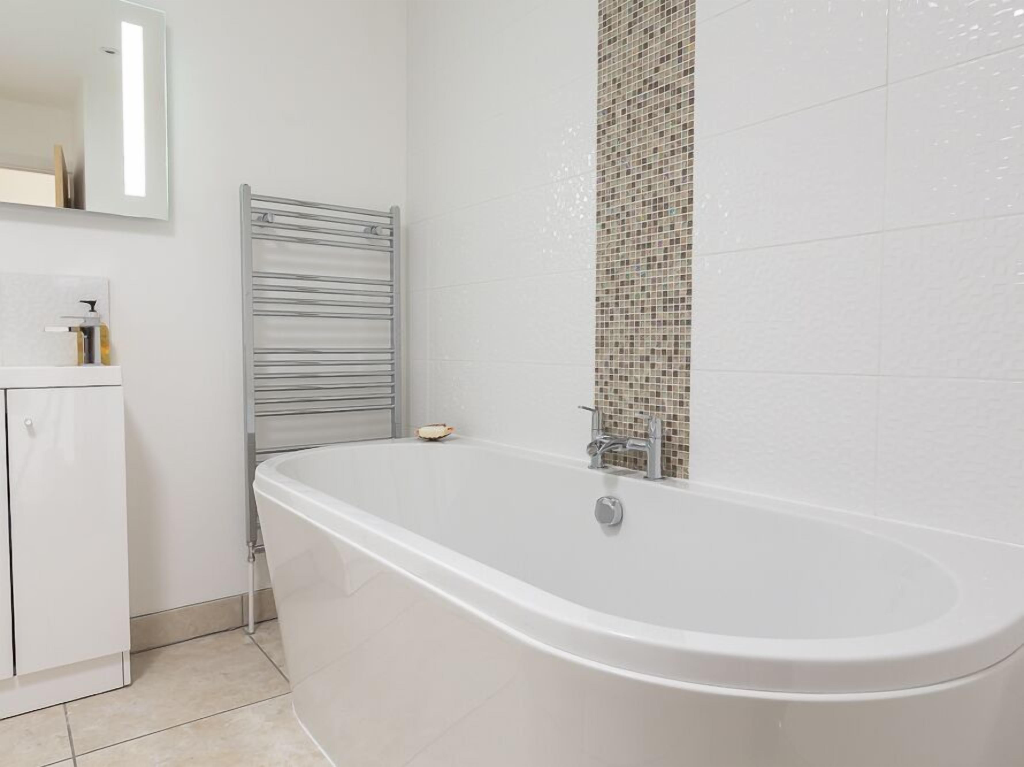 A modern bathroom with a freestanding bathtub, a towel rack, and a tiled wall with a mosaic pattern.
