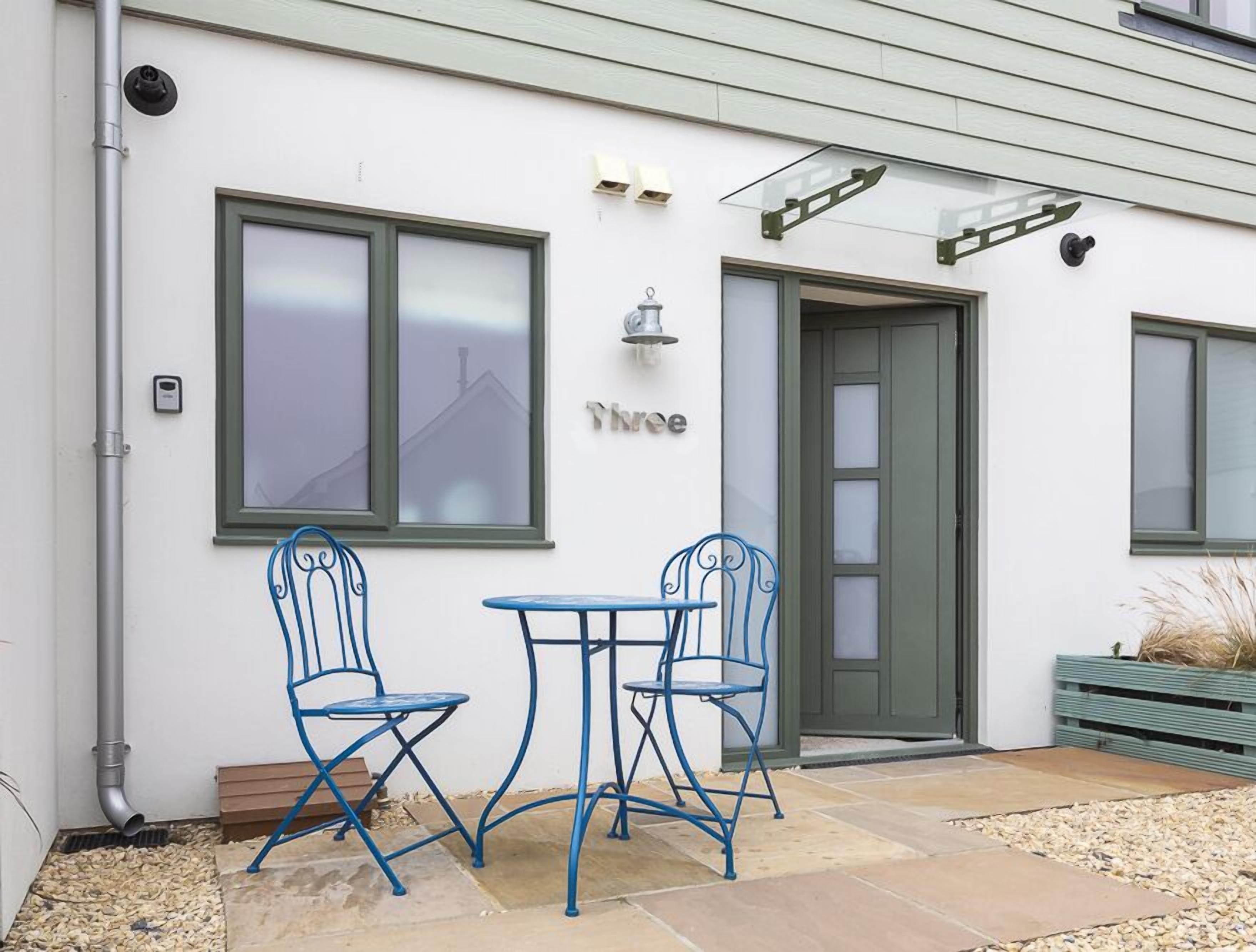A modern building with a white exterior, a green door, and a sign that reads "Three."