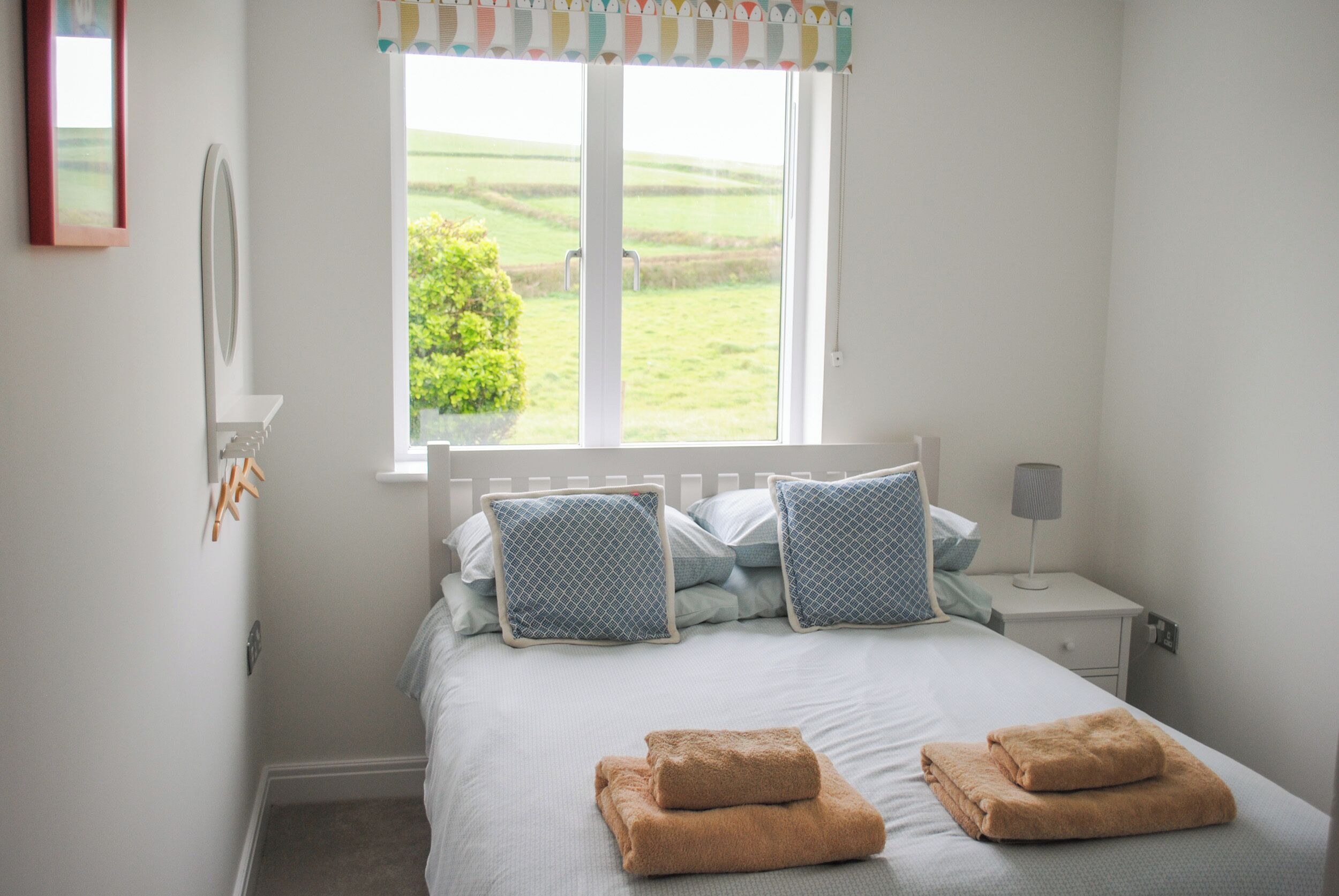 A bedroom with a bed, two pillows, a nightstand, a lamp, and a window with a view of greenery.