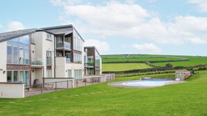 Une maison moderne à deux étages avec une piscine, entourée de champs verdoyants et de collines.