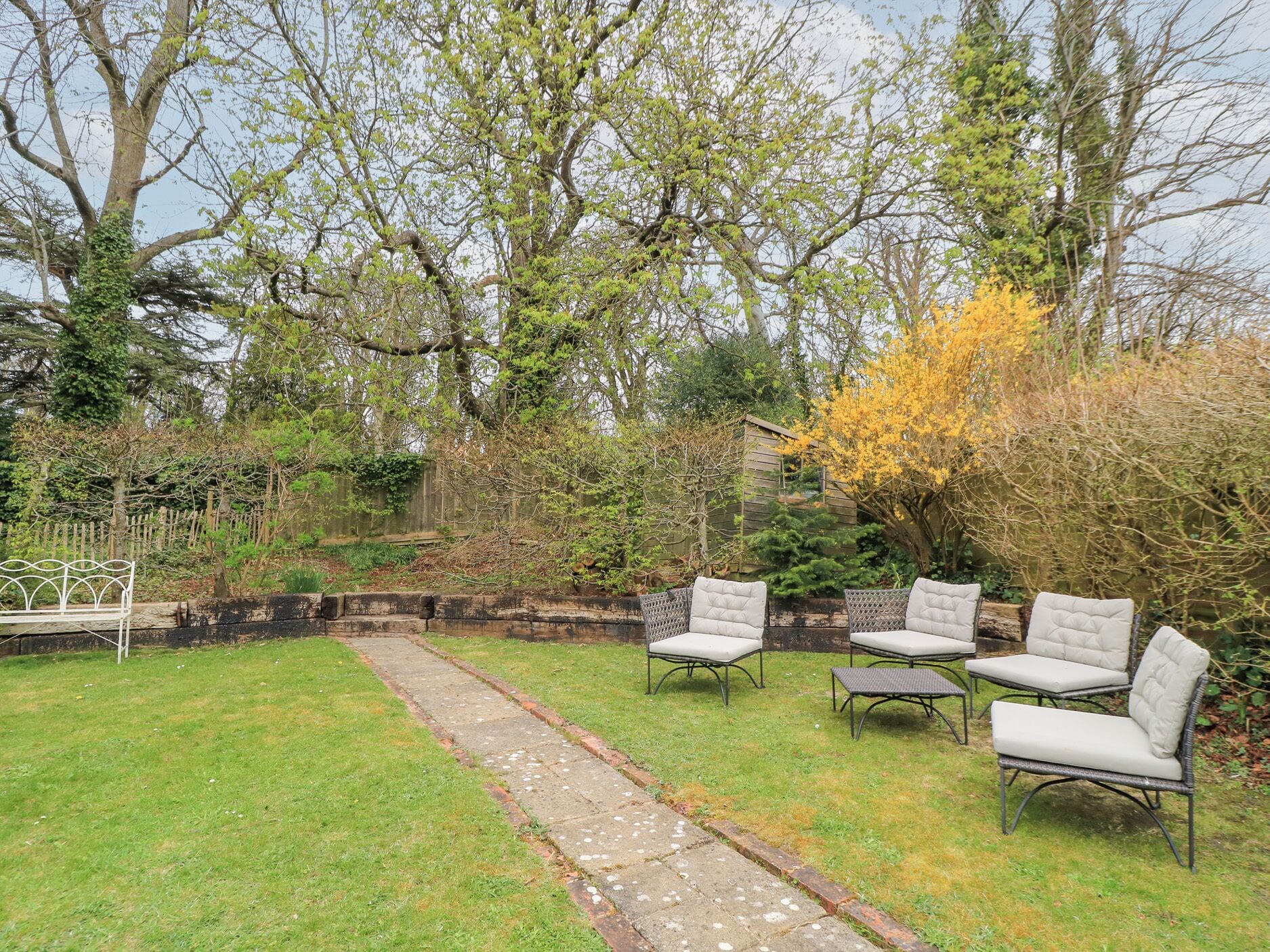 A garden with a paved pathway, outdoor seating, and trees.