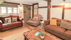 A cozy living room with a brown leather sofa, a patterned armchair, and a wooden coffee table with a plant. - Cosy Cot (Salisbury)