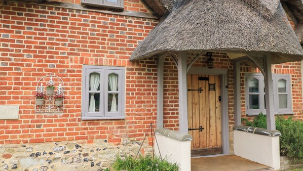 A traditional brick house with a thatched roof, a wooden door, and a small garden area with plants. - Cosy Cot (Salisbury)