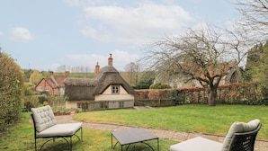 A thatched-roof house with a garden featuring a paved pathway, two outdoor seating areas, and a hedge. - Cosy Cot (Salisbury)