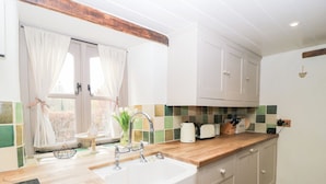 A kitchen with a sink, wooden countertop, white cabinets, and a window with curtains. - Cosy Cot (Salisbury)