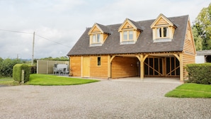 A two-story wooden house with a covered garage, a gravel driveway, and a well-maintained lawn. - Acorn Cottage (Ludlow)