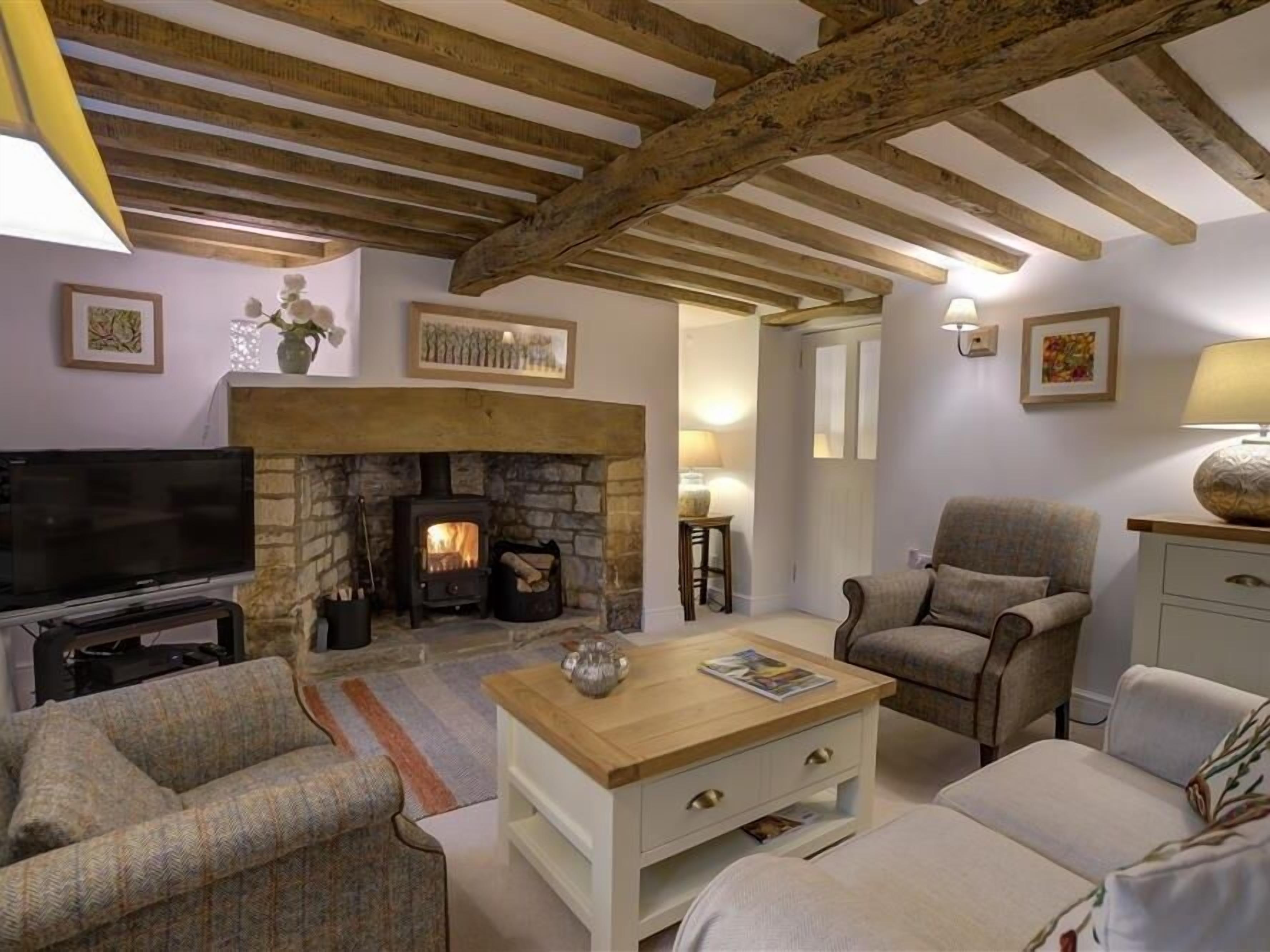 A cozy living room with a stone fireplace, wooden beams, a television, and comfortable seating.