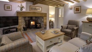 Un salon chaleureux avec une cheminée en pierre, des poutres en bois, un téléviseur et des sièges confortables.