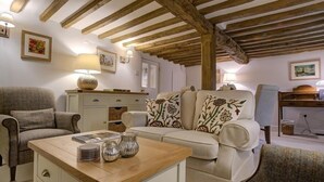 Un salon chaleureux avec un plafond en bois, un canapé agrémenté de coussins à motifs floraux, une table d’appoint ornée d’objets décoratifs et une lampe.