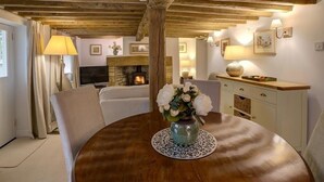 Une pièce chaleureuse avec un plafond en bois, une cheminée, une table à manger agrémentée d’un vase de fleurs et un téléviseur.