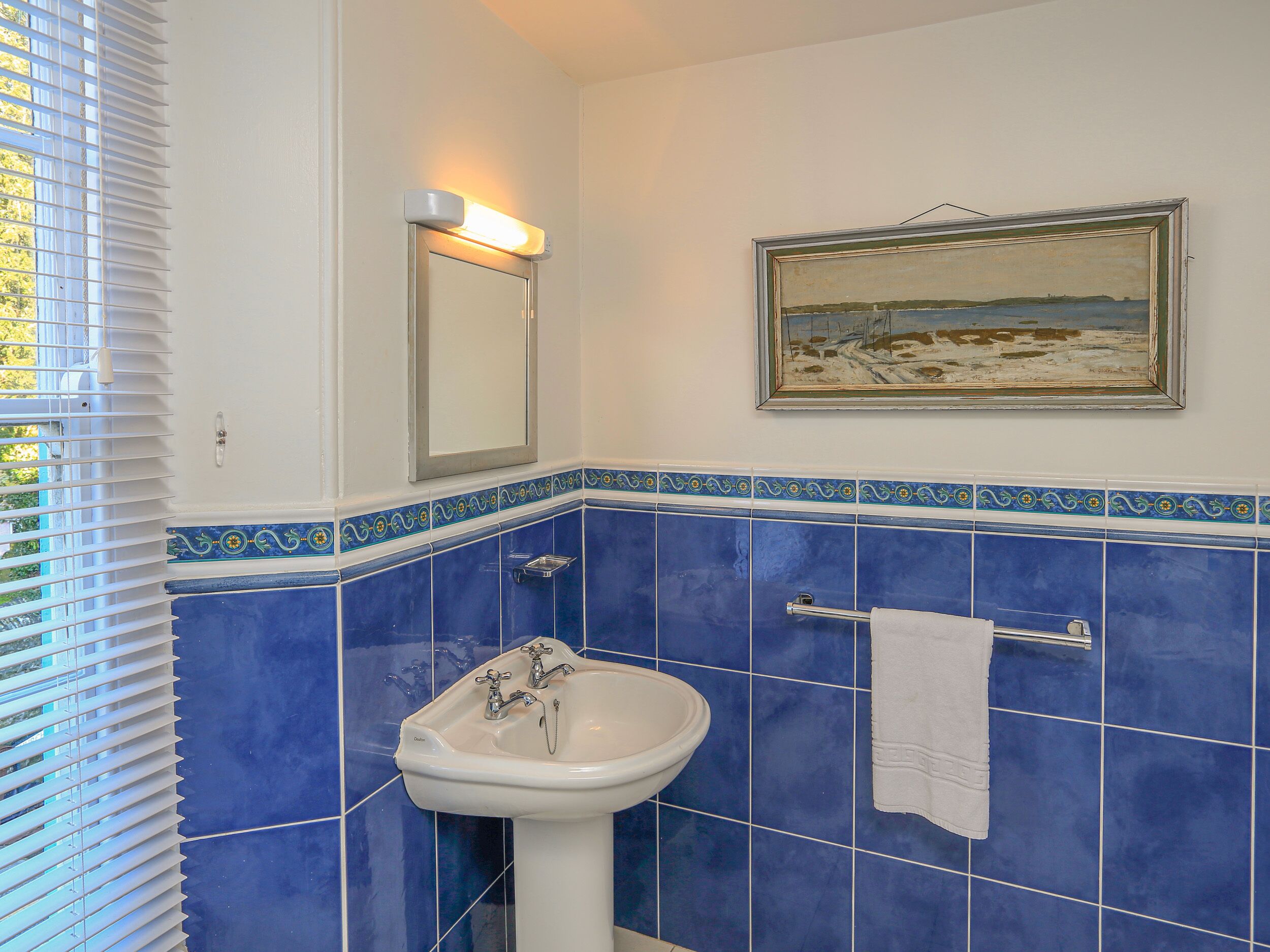 Een badkamer met een wastafel, spiegel en een schilderij aan de muur.