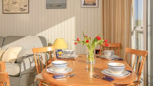 A dining area with a round wooden table set for four, surrounded by wooden chairs. There is a vase with red flowers on the table, and a lamp with a yellow shade. - Upper Marcam House (Salcombe)