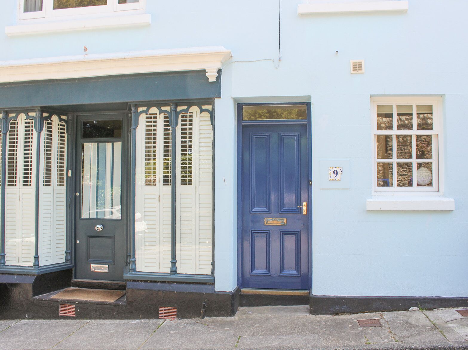A blue house with a dark blue door, a white window, and a small white plaque with the number 9.