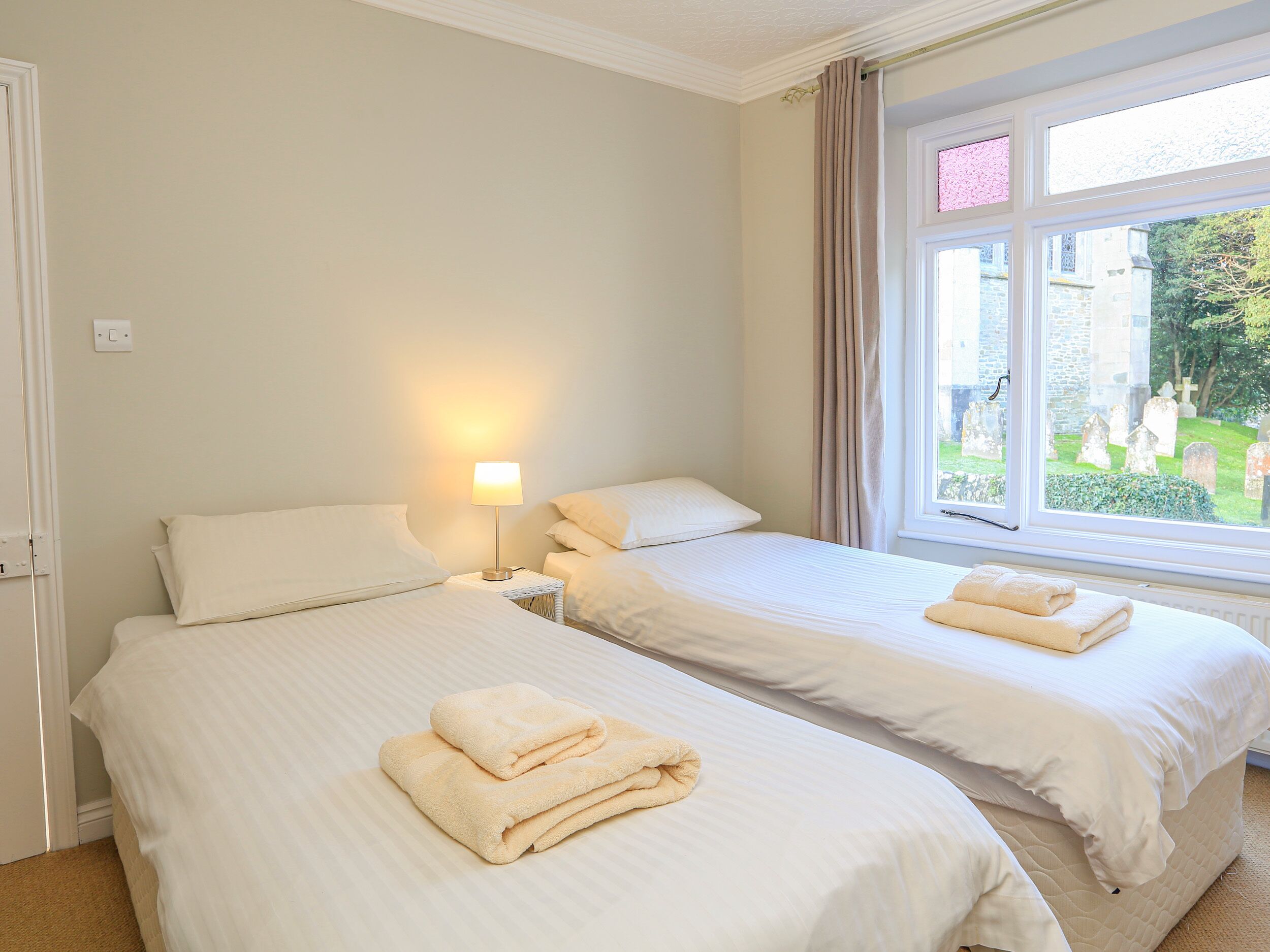 A hotel room with two beds, a bedside lamp, and a window with a view of a cemetery.