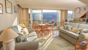 A spacious living room with a large sofa, a dining table, and a balcony with a view. - Upper Marcam House (Salcombe)