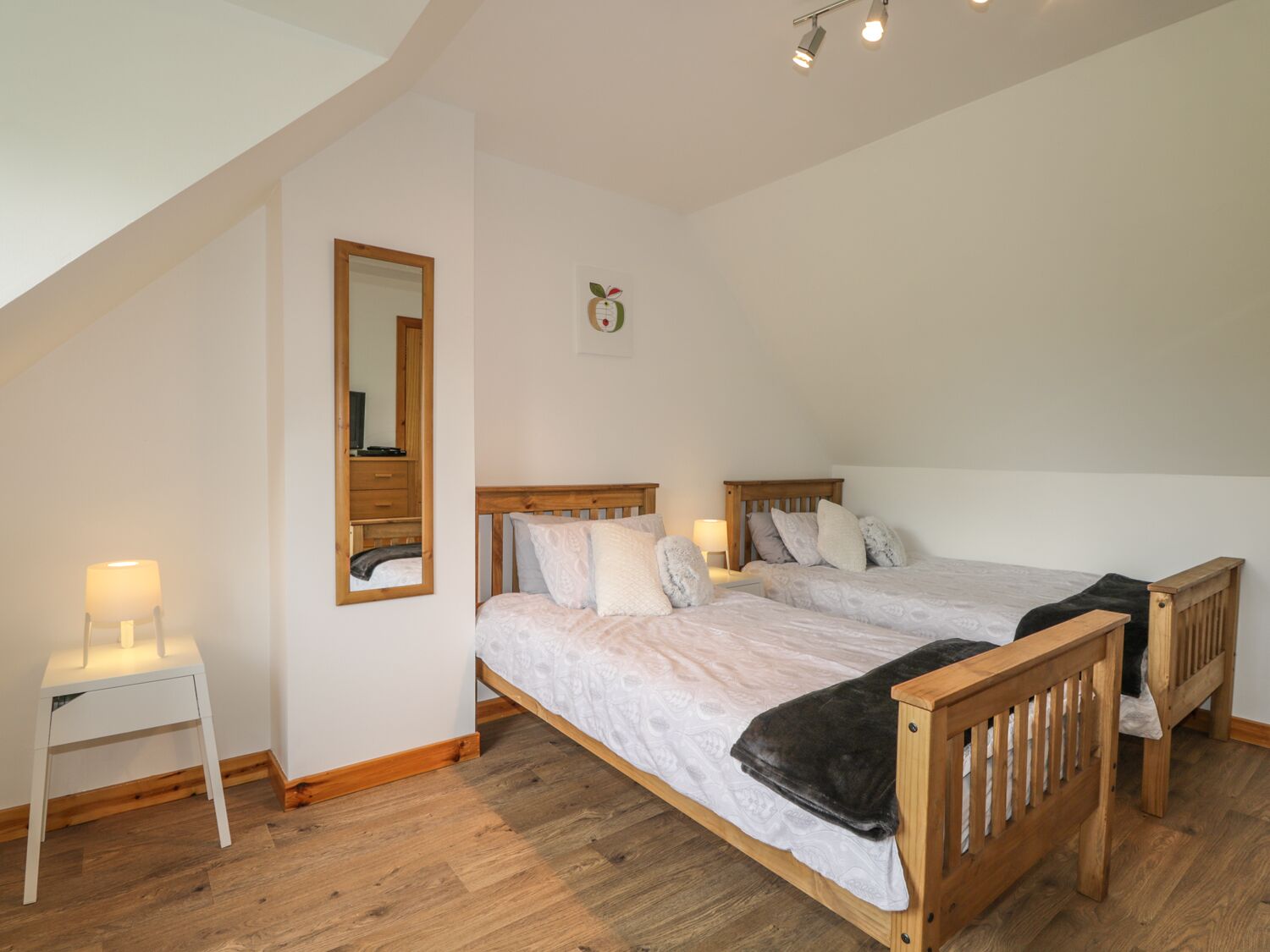 A bedroom with two wooden beds, a white bedside table, a mirror, and a small wall decoration.