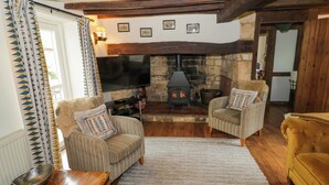 A cozy living room with a fireplace, two striped armchairs, a yellow sofa, and a wooden ceiling. - Elmhurst Cottage (Stratford-upon-Avon)