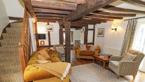 A cozy living room with a sofa, armchairs, a coffee table, and a staircase. - Elmhurst Cottage (Stratford-upon-Avon)
