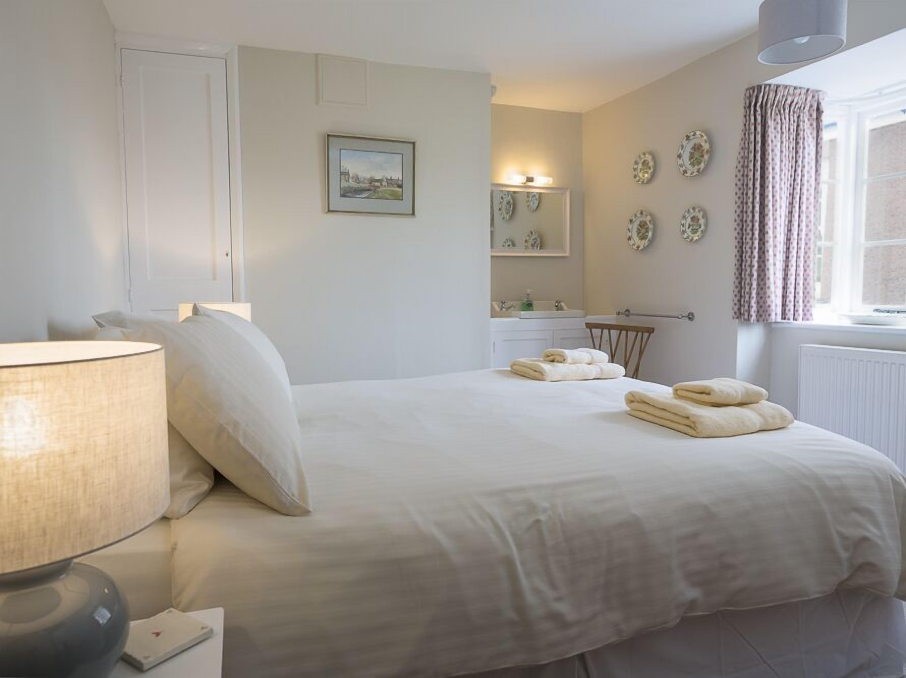 Une chambre bien rangée, avec un lit, une lampe de chevet et une fenêtre avec des rideaux.