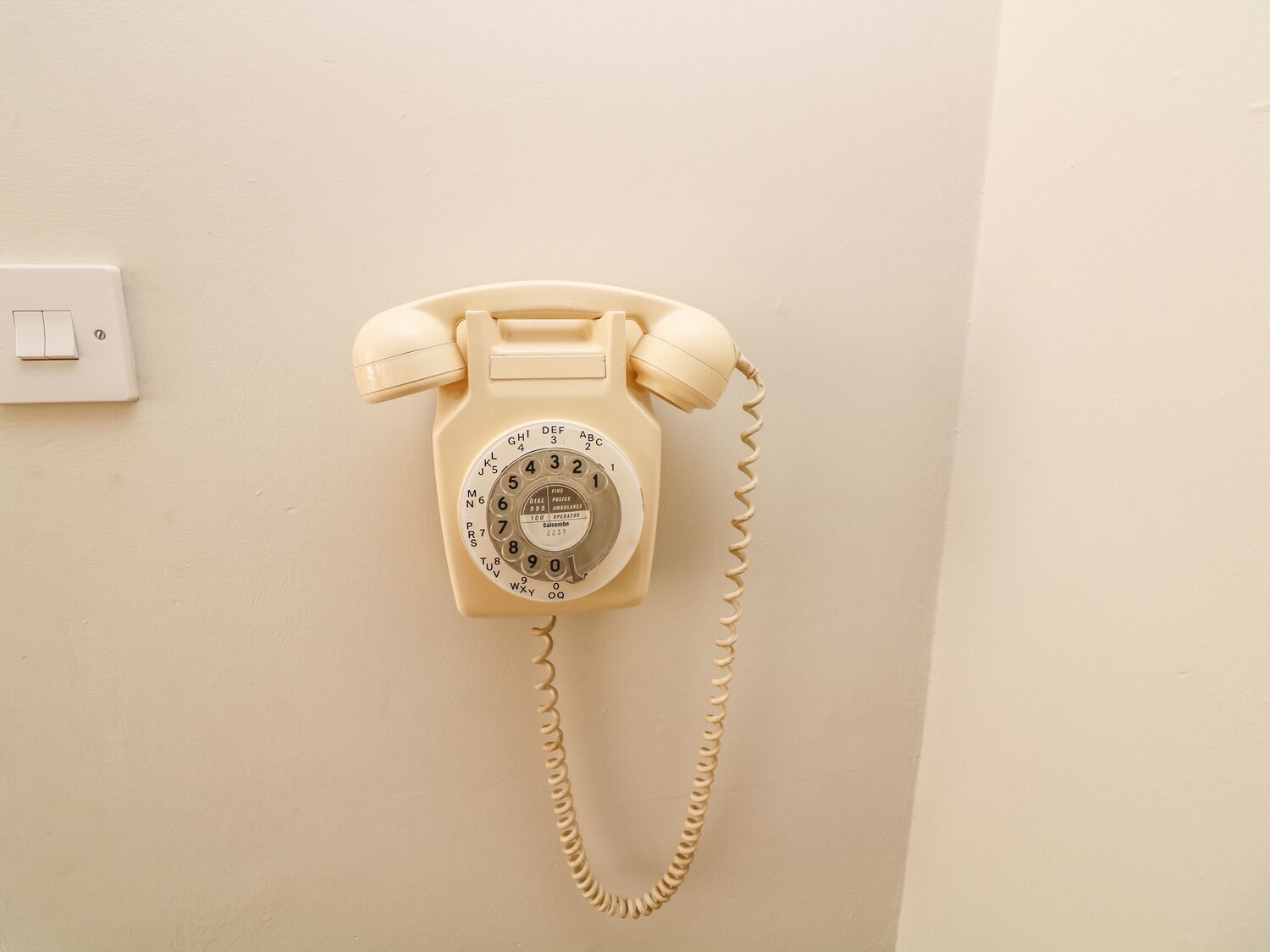 A beige rotary dial telephone mounted on a wall with a coiled cord.