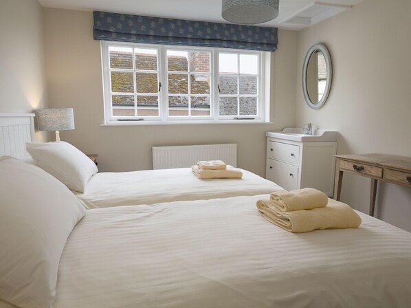 Une chambre avec deux lits, une fenêtre donnant sur un beau paysage, une table de chevet, une commode et un miroir.