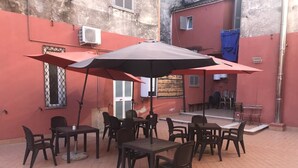 An outdoor patio with multiple tables and chairs, a large umbrella, and a tiled floor. - Old Bakery Guest house (Rome)