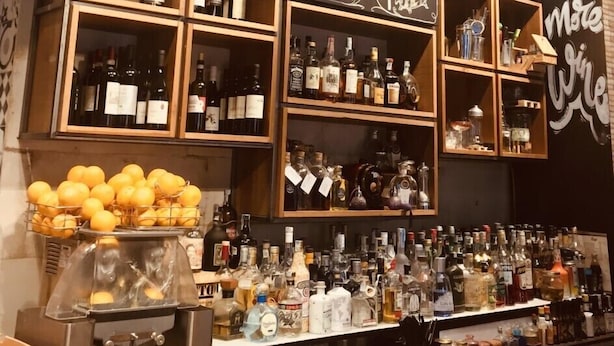 A bar area with shelves of liquor bottles, a fruit display, and chalkboard menus listing drinks and prices. - Old Bakery Guest house (Rome)