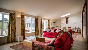 A spacious living room with a red sofa set, a glass coffee table, and a view of the outdoors through large windows. - Wytons Piece (Shipston on Stour)
