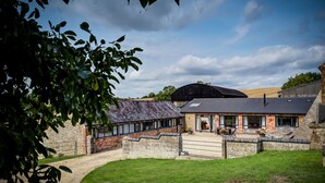 A rustic barn-style building with a stone exterior, a large open porch, and a gravel driveway. - Wytons Piece (Shipston on Stour)