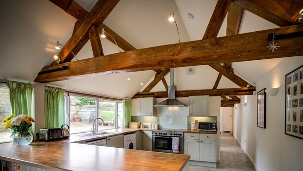 A kitchen with wooden beams, a central island with stools, a washing machine, and a stove. - Wytons Piece (Shipston on Stour)