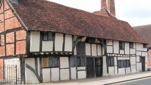 A traditional half-timbered building with a steeply pitched roof and a gated entrance. - One Masons Court (Stratford-upon-Avon)