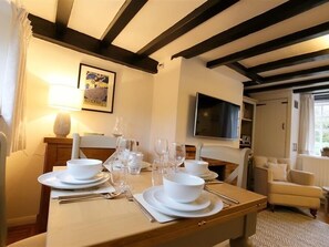 A dining area with a table set for four, a television mounted on the wall, and a cozy seating area with a chair. - One Masons Court (Stratford-upon-Avon)
