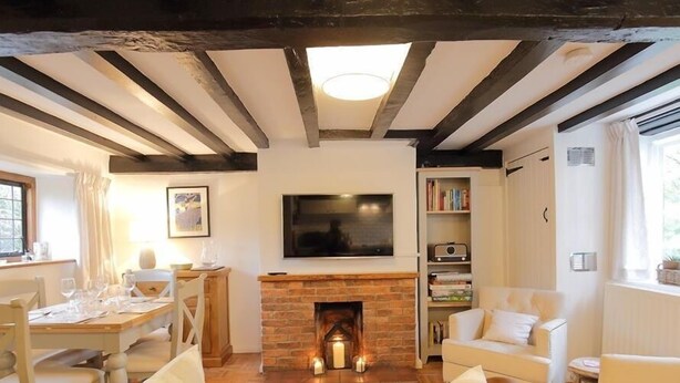 A cozy living room with a fireplace, a television mounted on the wall, and a dining area with a table set for four. - One Masons Court (Stratford-upon-Avon)