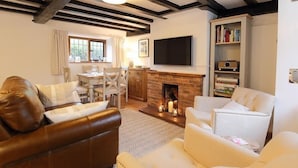 A cozy living room with a fireplace, leather sofa, and white armchairs. - One Masons Court (Stratford-upon-Avon)