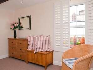 A room with a wooden dresser, a wicker chair, a window with blinds, and a framed mirror on the wall.