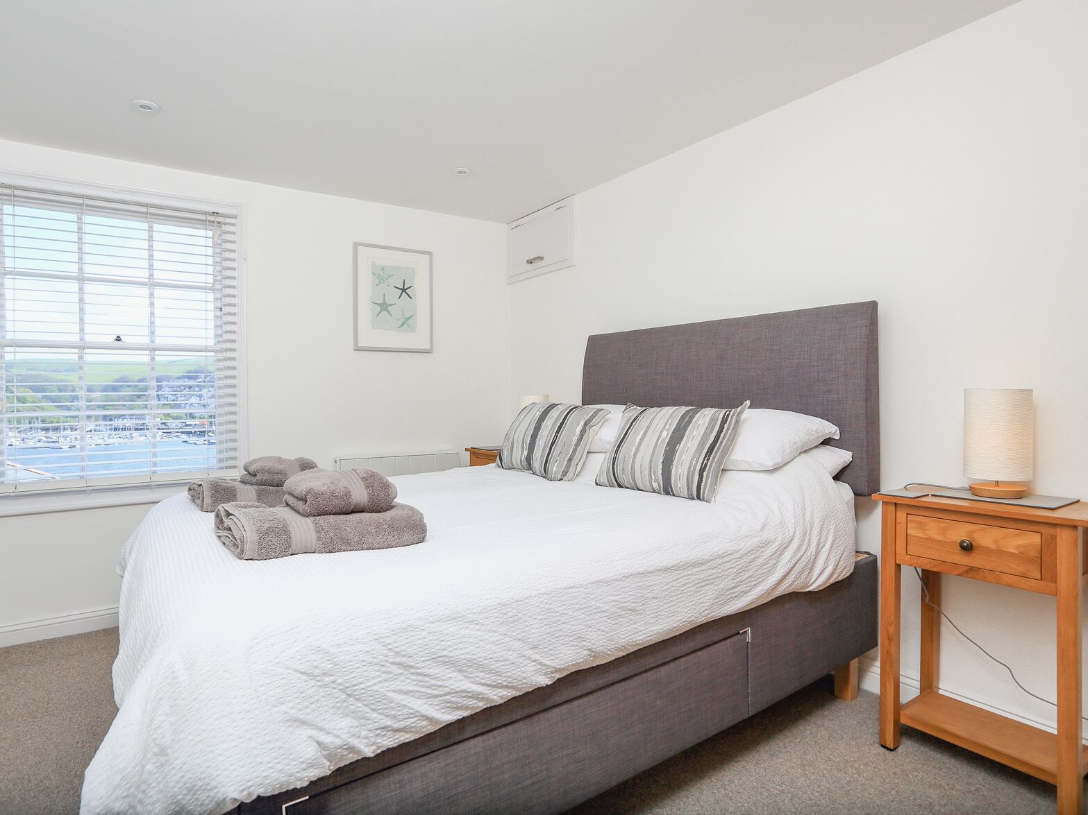 Une chambre à coucher avec un lit, une table de chevet, une lampe et une fenêtre avec des stores.