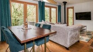Un amplio salón con una mesa de comedor de madera, sillas tapizadas en azul, un sofá gris y un televisor montado en la pared.