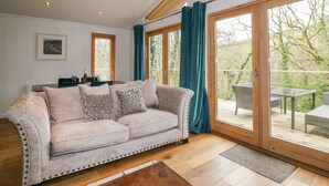 Una sala de estar acogedora con un sofá color beige, vigas de madera, ventanas amplias y vistas al exterior.