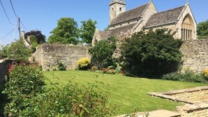 A historic stone building with a tower, surrounded by a well-maintained garden and stone walls. - Hillside Cottage (Burford)